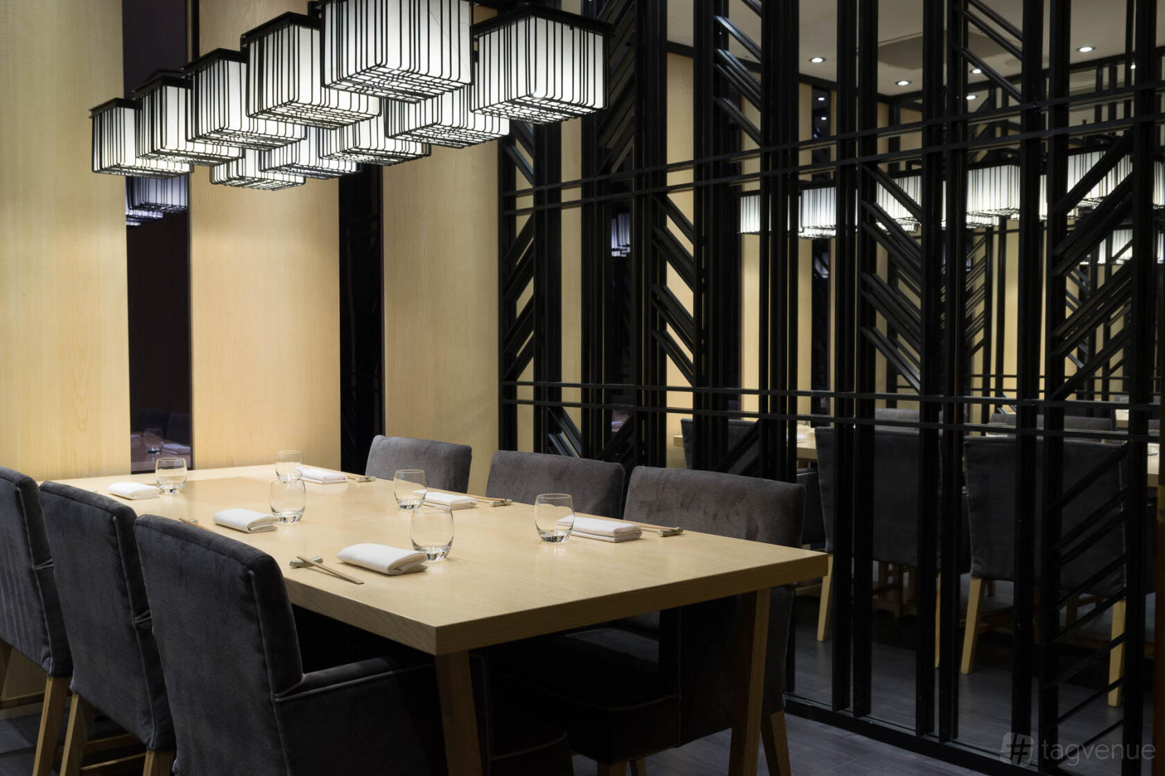 A restaurant dining room with a light wood table, grey velvet chairs, and geometric mirrored walls at Ginza St. James's.