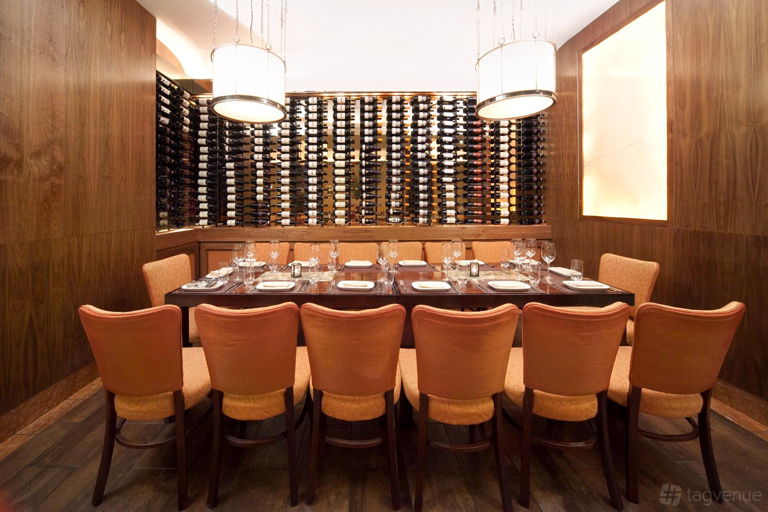 An event space in a restaurant with a long dining table, orange chairs, and a wall of wine bottles at Pera Mediterranean Brasserie.