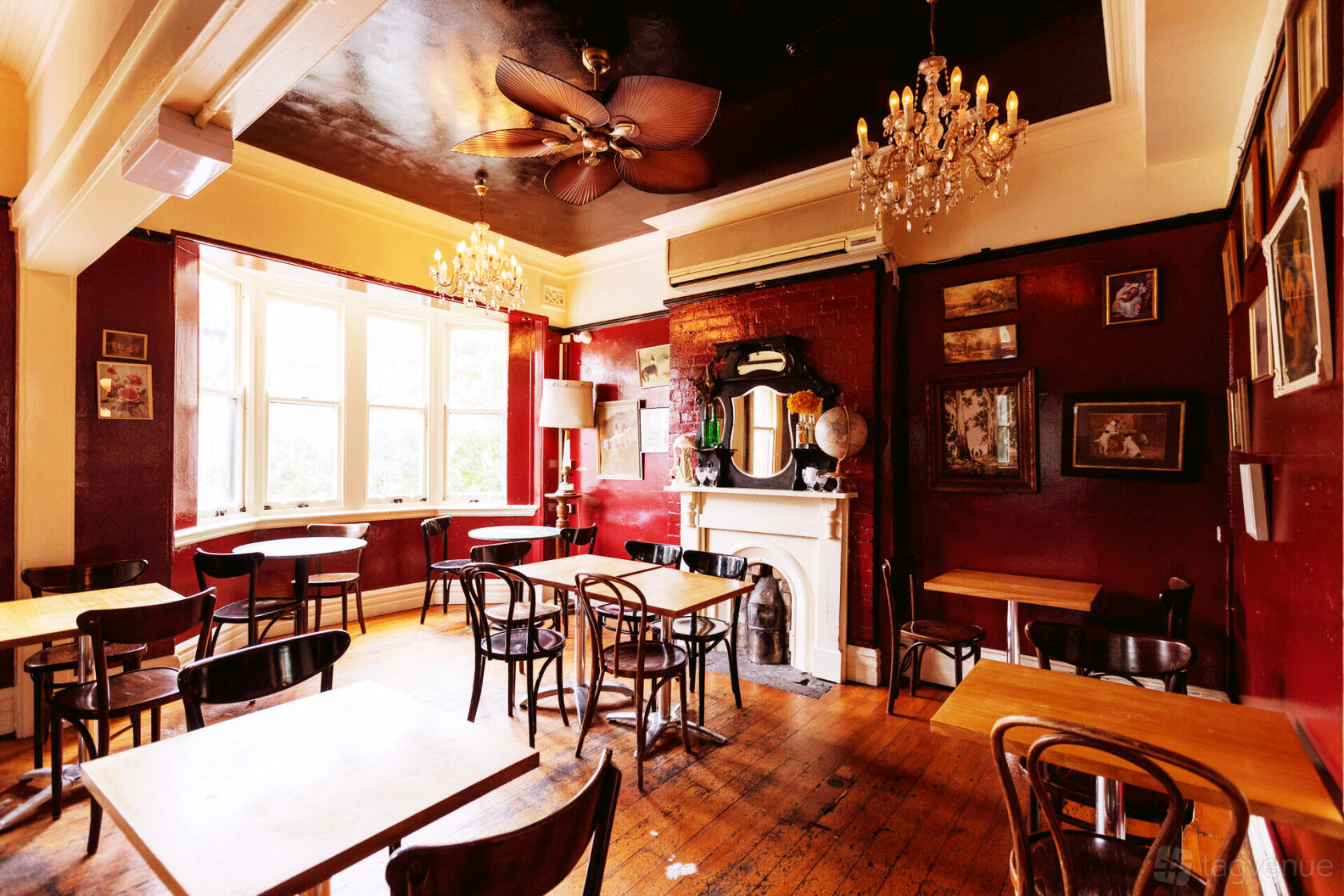 An event space in a pub with wooden floors, red walls, chandeliers, and a decorative fireplace at The Old Fitzroy Hotel.