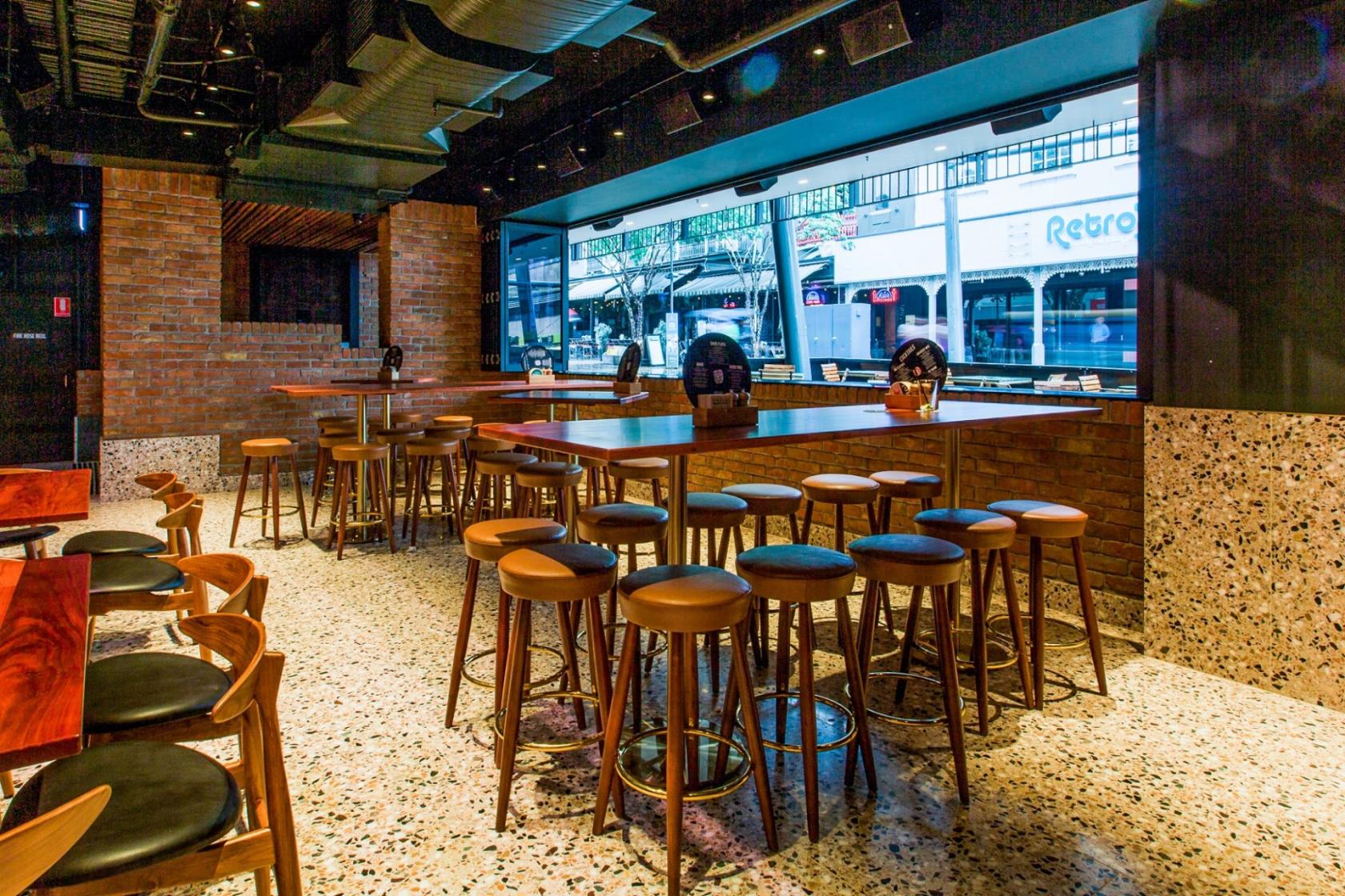A dining room with brick walls, terrazzo flooring, high tables, and large street-facing windows at The Sound Garden.