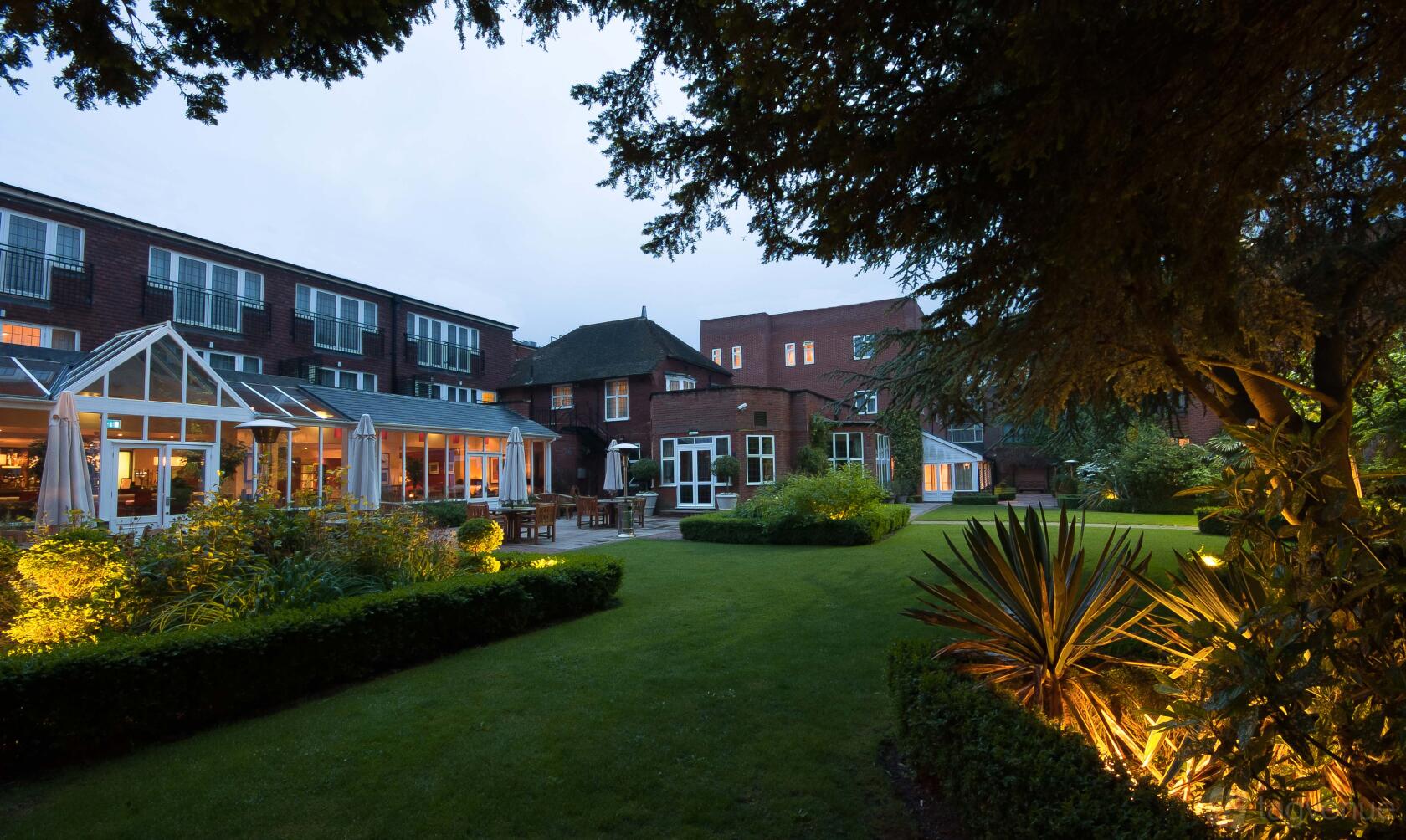 A hotel with a landscaped garden, outdoor seating, and conservatory windows at The Bull Hotel.
