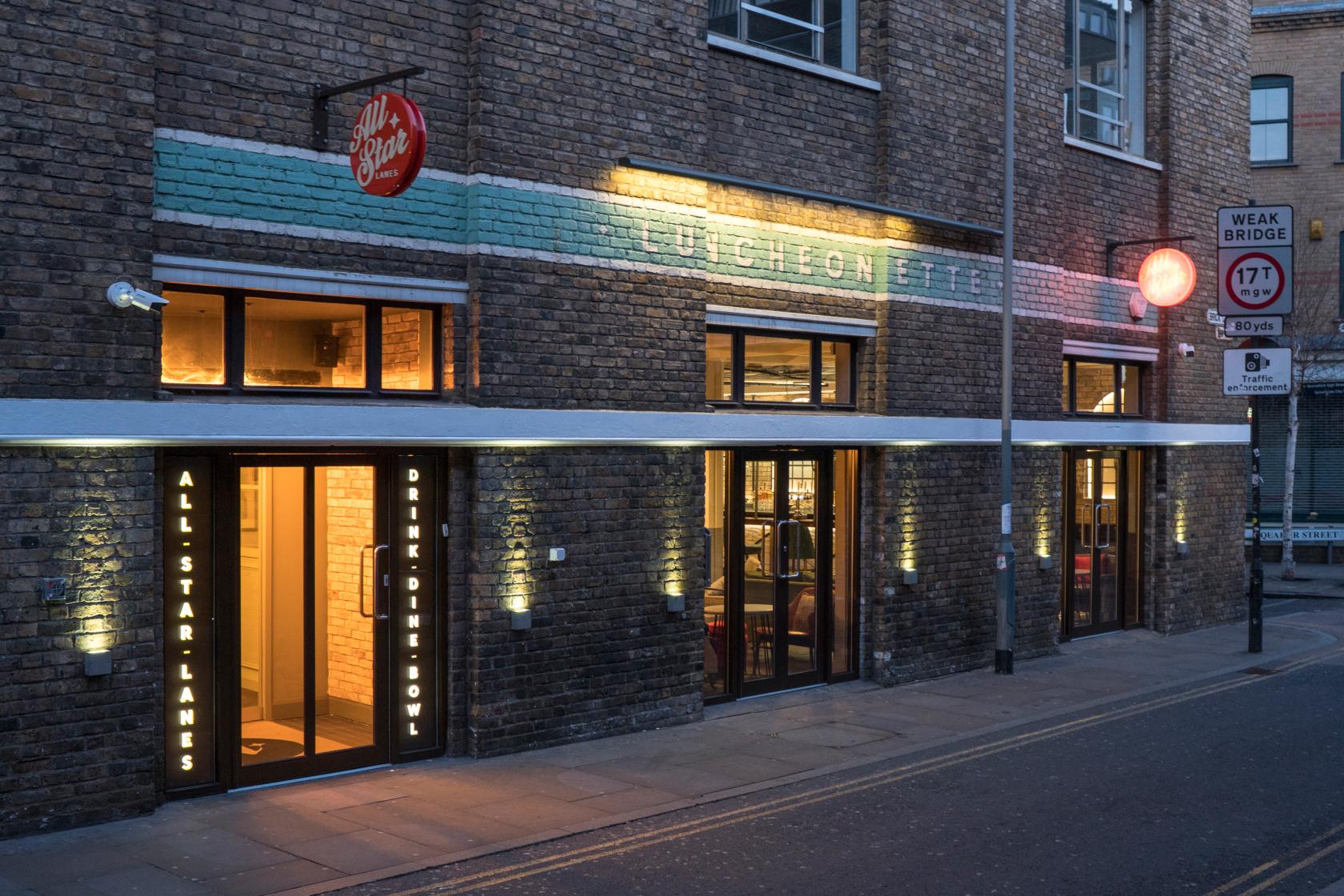 A bowling alley with brick exterior, large windows, and illuminated signage at All Star Lanes Brick Lane.