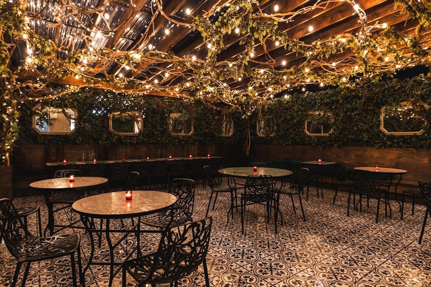 A restaurant terrace with wrought iron tables, patterned tile floors, and overhead string lights at SAINT.