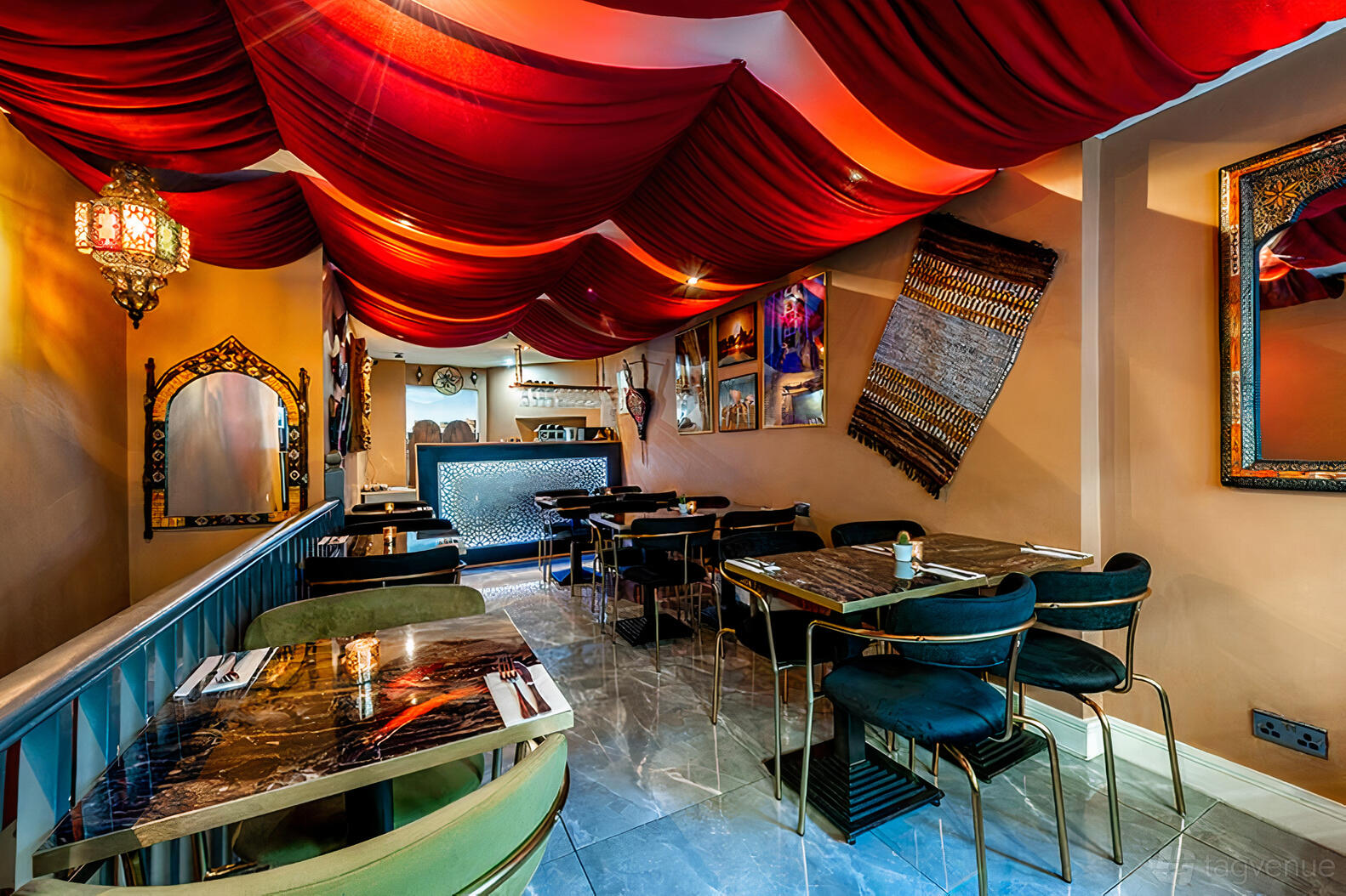 A restaurant with red draped ceiling fabric, marble-top tables, and Moroccan decor at Bab Mansour.