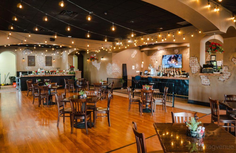 An event space in a bar with wooden floors, string lights, exposed brick accents, and small tables at Chill Bar Grill.
