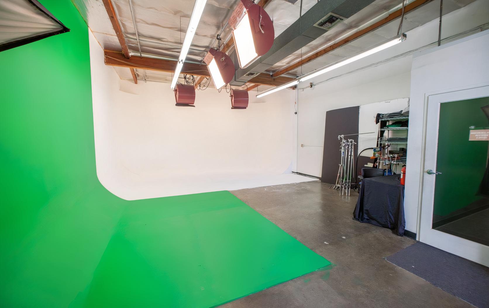 A photo studio with a green screen backdrop, white cyclorama wall, and overhead studio lighting at AMG Studios.