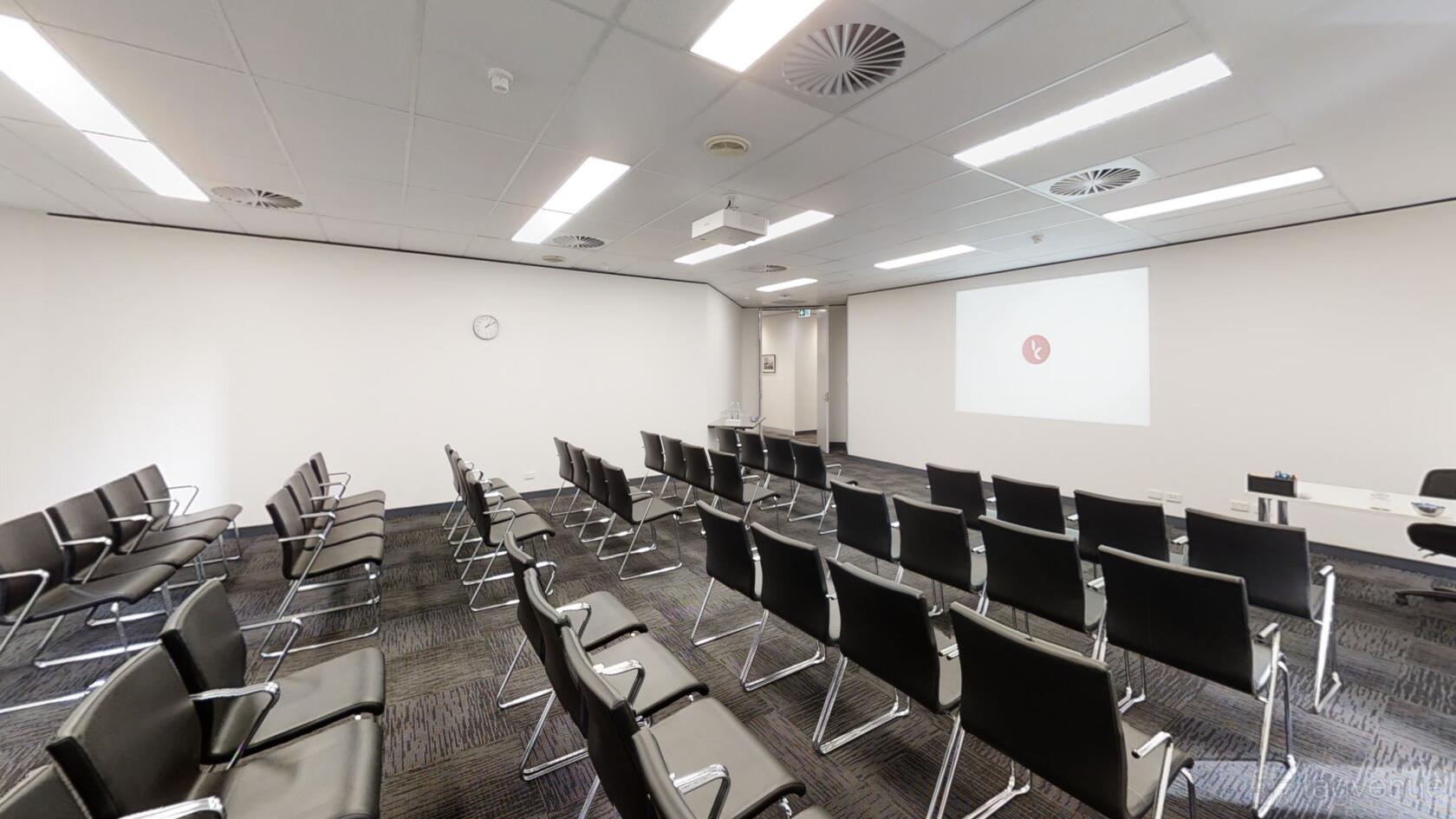 A conference centre room with rows of black chairs, a projector, and a large screen at Karstens Perth.