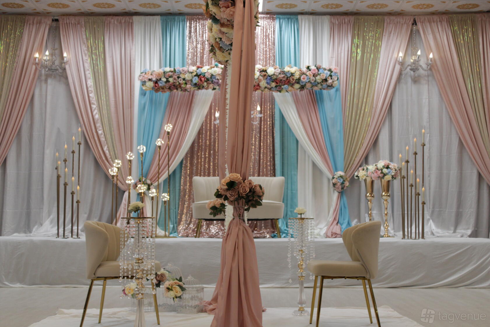 A banqueting hall with pastel draped curtains, floral arrangements, and gold candle stands at Chef Kausar's Autaq Banquet Hall.