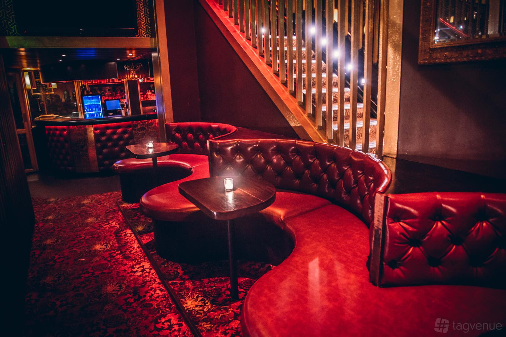 An event space in a nightclub with red tufted leather booths, candlelit tables, and a carpeted floor at Onesixone.