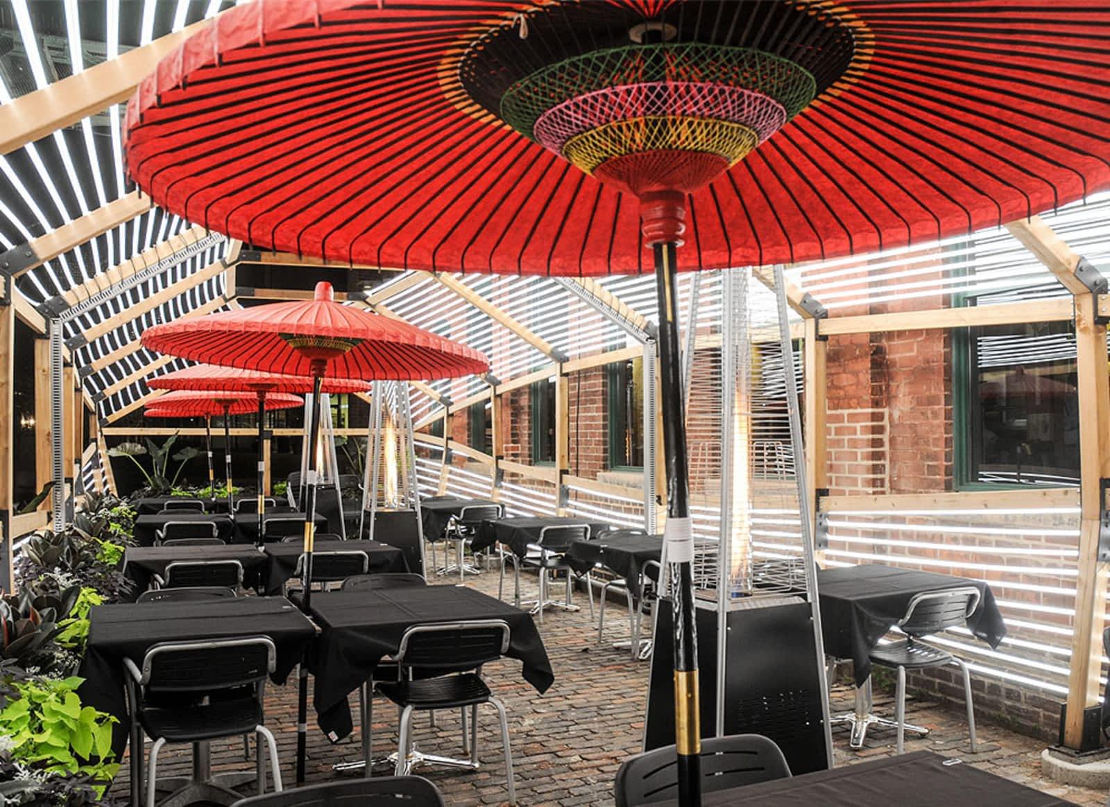 An outdoor restaurant patio with red parasols, black tablecloths, and wooden pergola at BOKU Japanese Eats + Drinks.