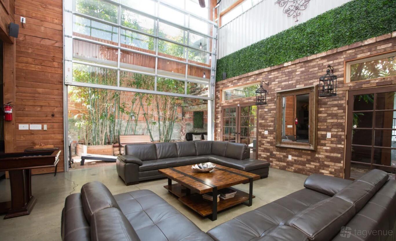 A loft with floor-to-ceiling windows, exposed brick walls, and leather sofas arranged around a coffee table at Bamboo Loft.