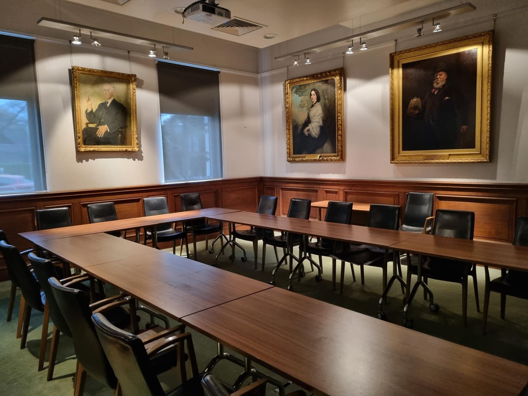 A meeting room with U-shaped wooden tables, black chairs, and classic portraits on the walls at ZSL London Zoo.