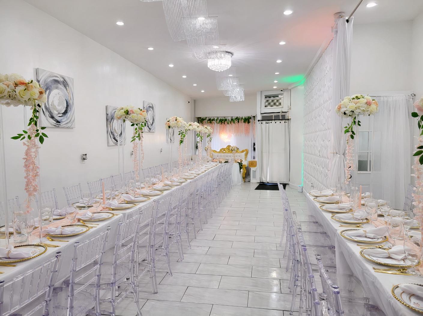 An event venue with long banquet tables, clear chairs, white floral centerpieces, and white draped walls at Aj's Event Parlour.