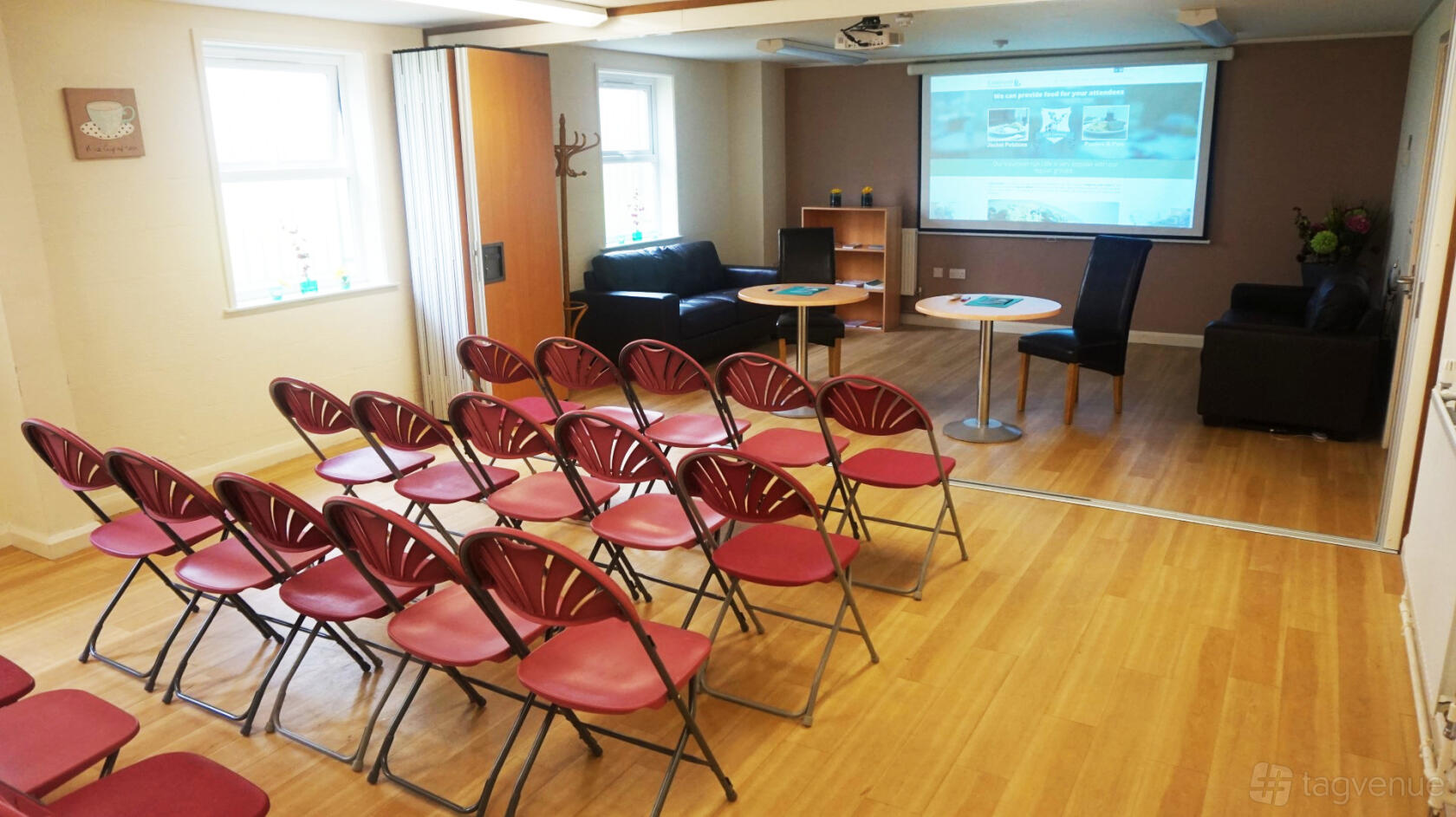 A community centre room with rows of red folding chairs, a projector screen, and wooden floors at Castleland Community Centre.