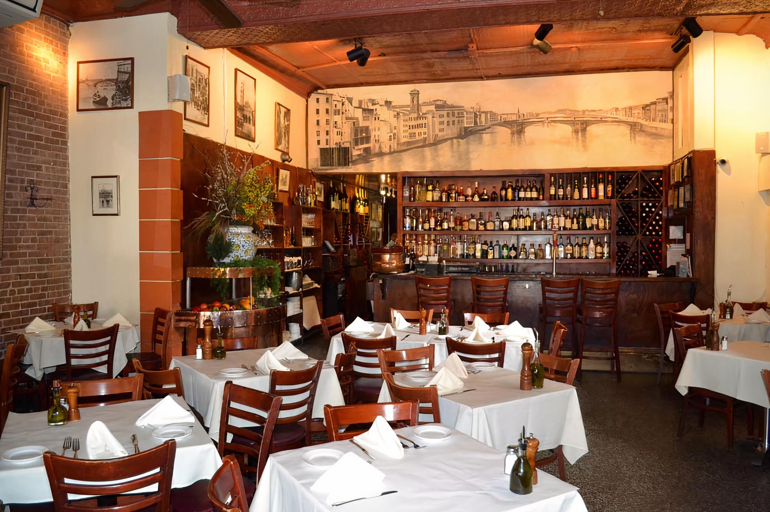 An event space in a restaurant with white linen-covered tables, wooden chairs, brick walls, and a mural at Pappardella.