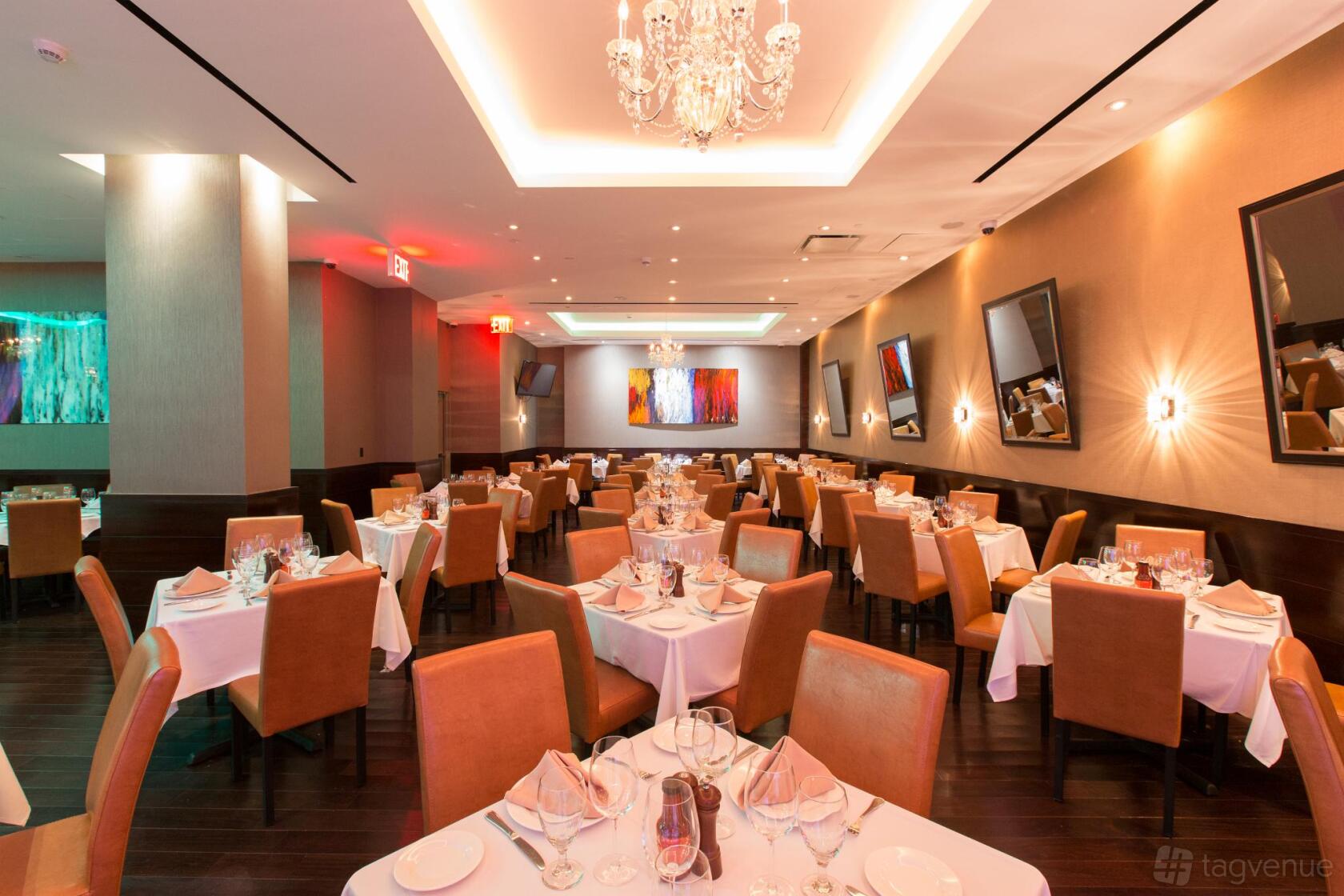 A private dining room with chandeliers, framed wall art, and round tables with white linens at Empire Steak House West.