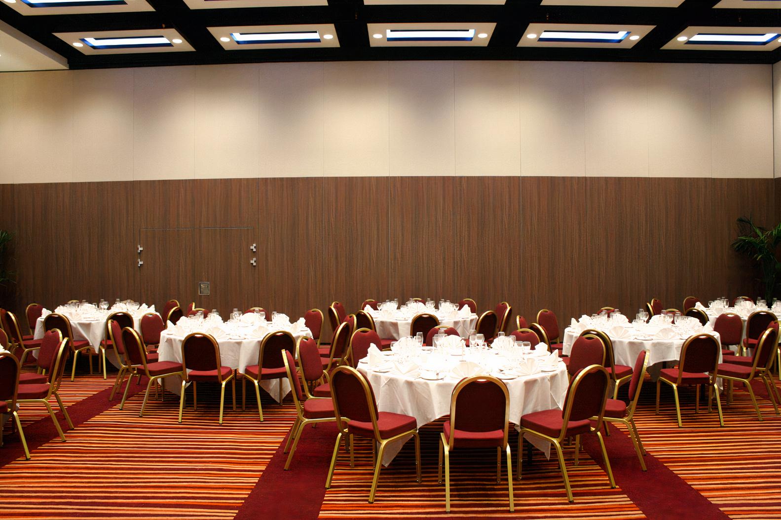An event space with round tables covered in white linens and red cushioned chairs at Mercure London Earl's Court.