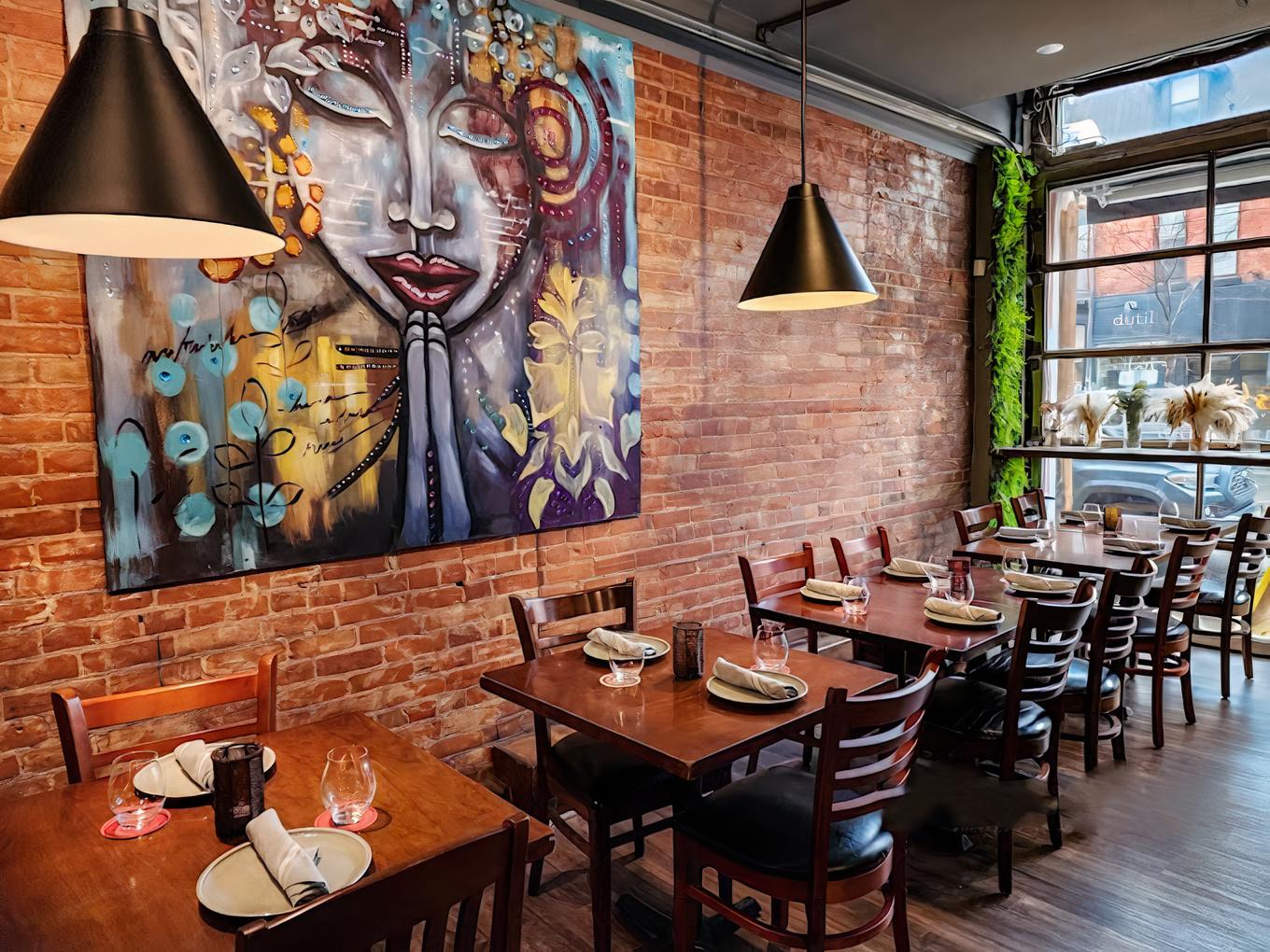 A restaurant with exposed brick walls, colorful artwork, pendant lighting, and wooden tables at Curryish Tavern.