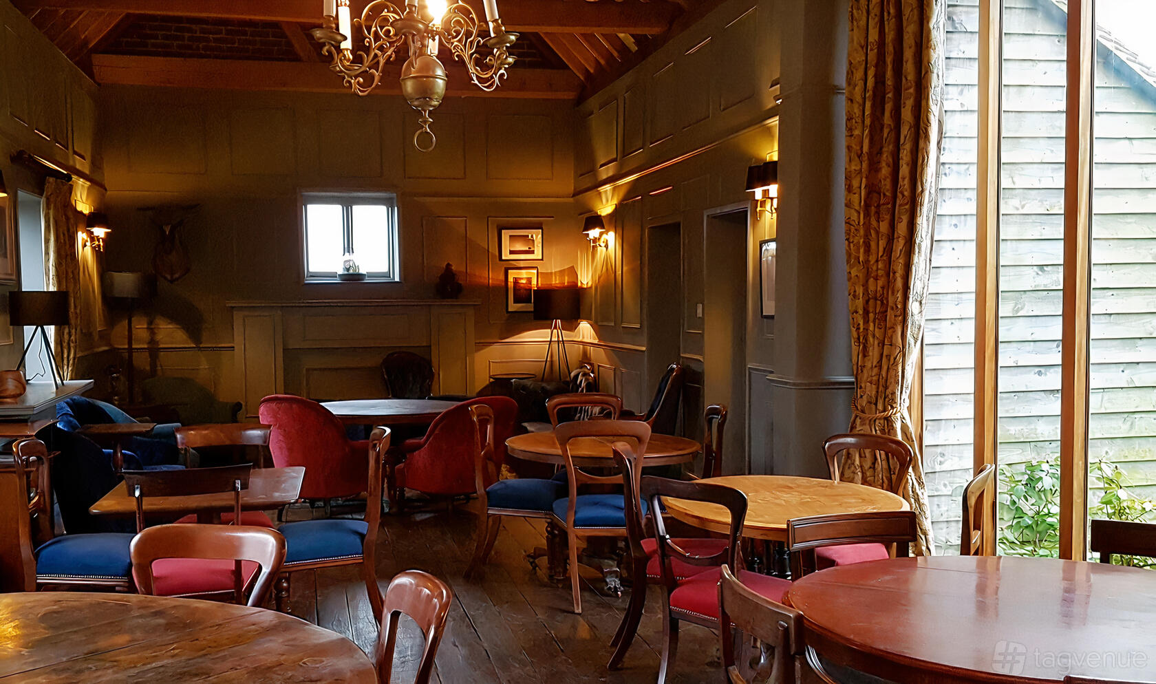 A country house lounge with round wooden tables, upholstered chairs, chandelier lighting, and large windows at Fair Oak Farm.