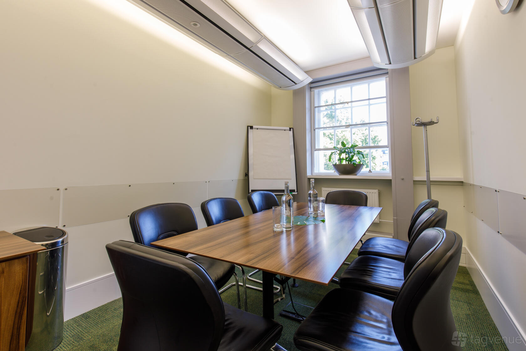 A meeting room with a rectangular wooden table, black chairs, flip chart, and a large window at 20 Cavendish Square.