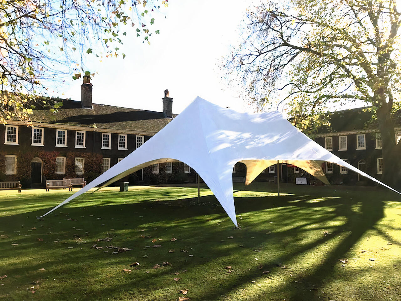 An event lawn with a large white stretch tent and mature trees at the Museum of the Home.
