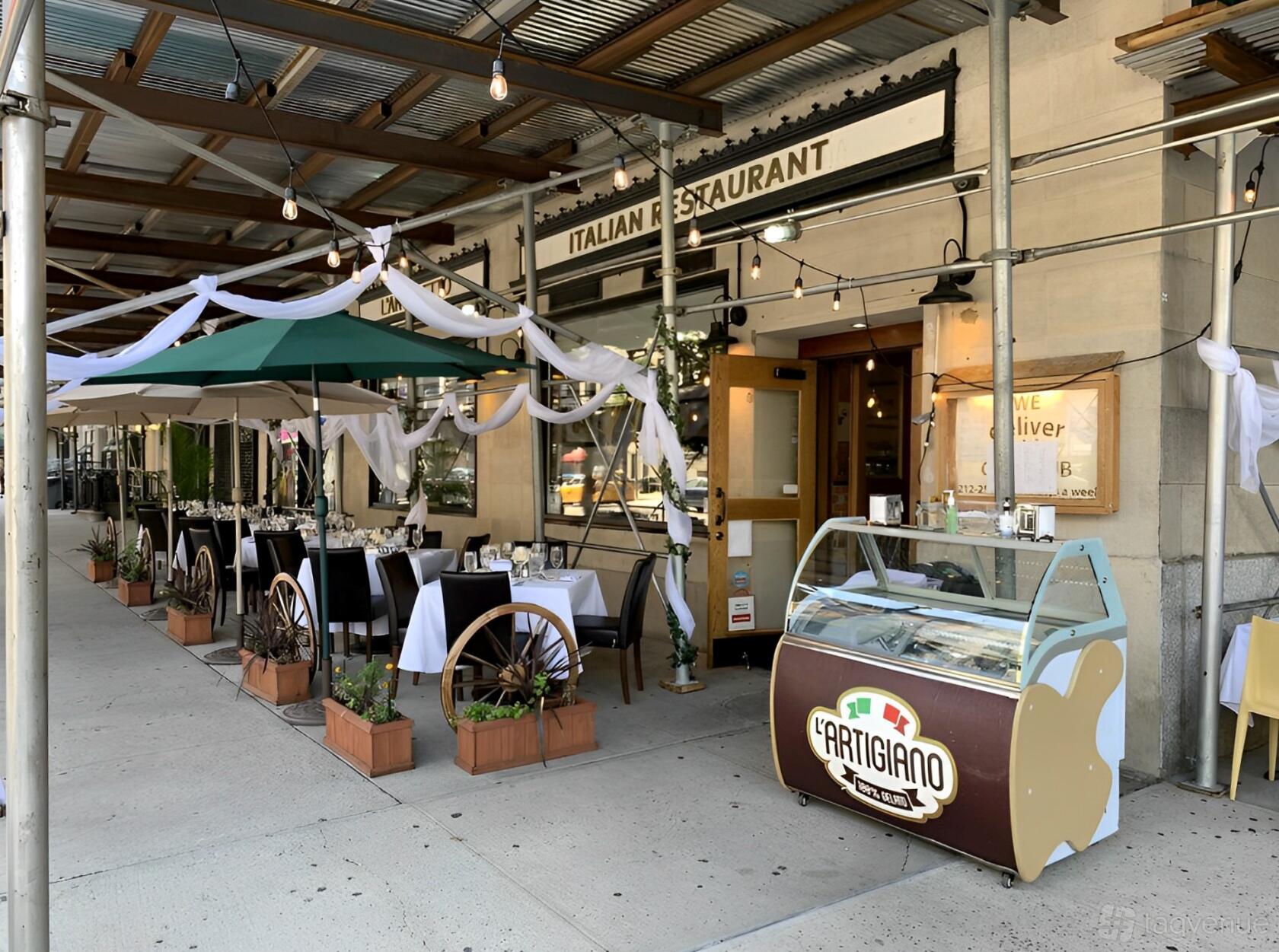 An outdoor restaurant seating area with white tablecloths, string lights, and an ice cream cart at L'Angeletto.