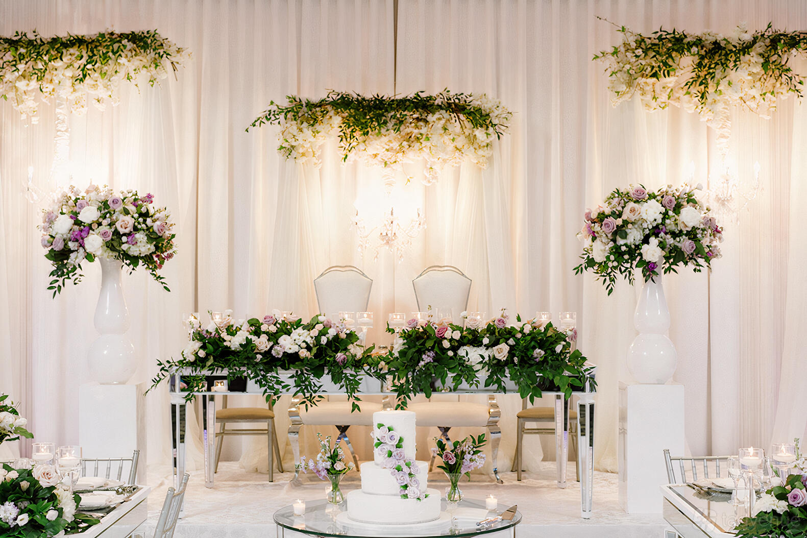 An event hall with draped white curtains, floral centerpieces, and a decorated dessert table at Parkview Manor.