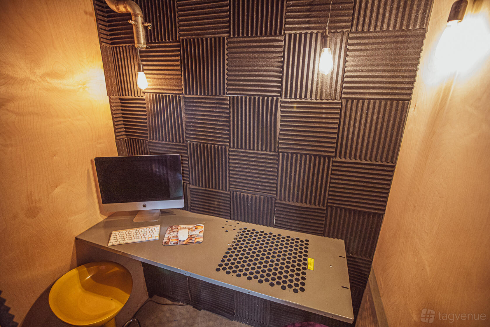 A small meeting room with foam acoustic panels, hanging lights, and a desk with a computer at PodShare San Diego.