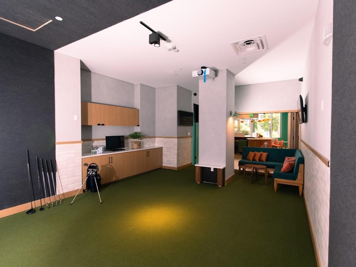 An event space with green carpet, golf clubs, a wall-mounted screen, and lounge seating at CitySwing.
