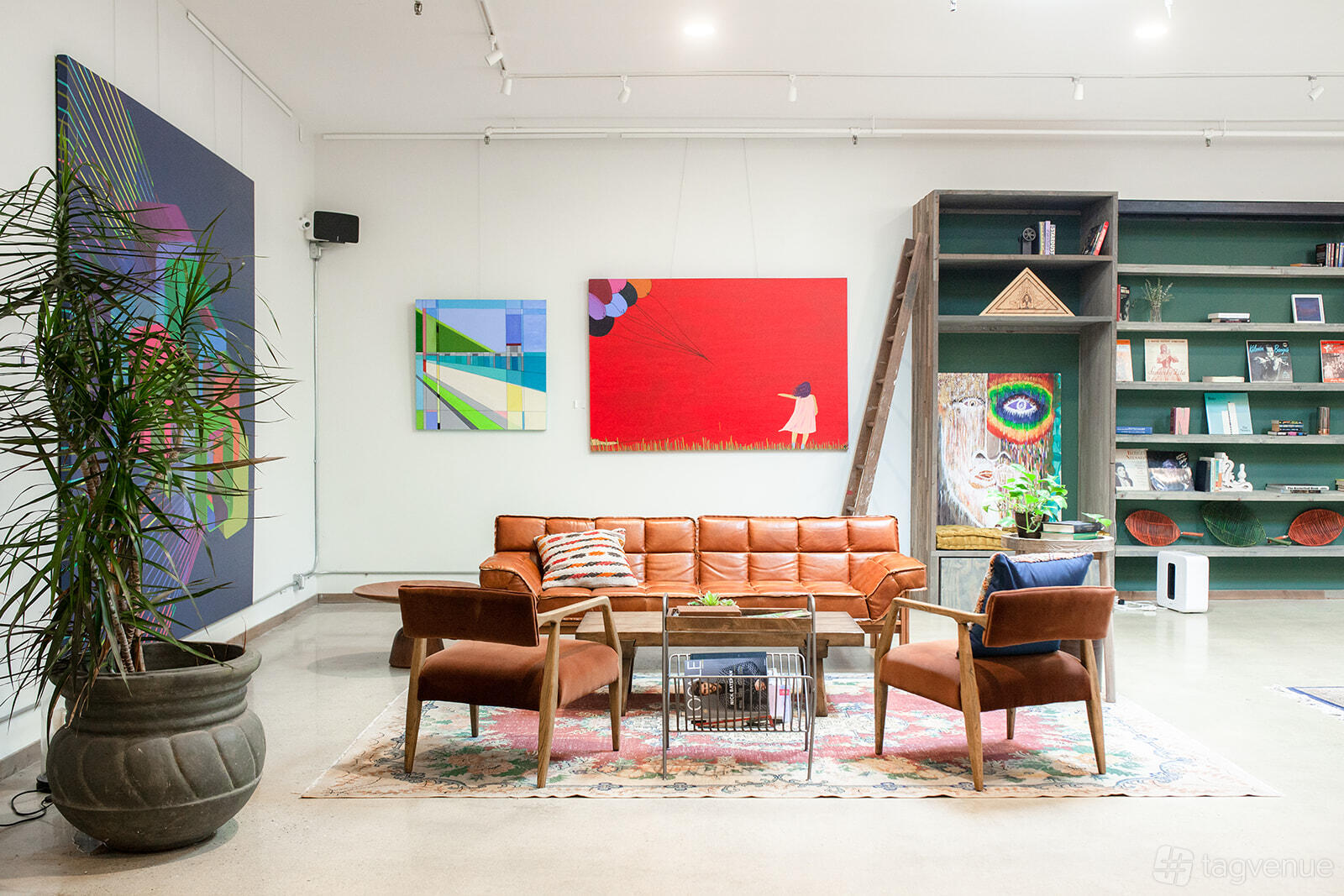 A library with leather lounge seating, colorful artwork, potted plants, and wall-mounted bookshelves at Unita Manhattan Beach.