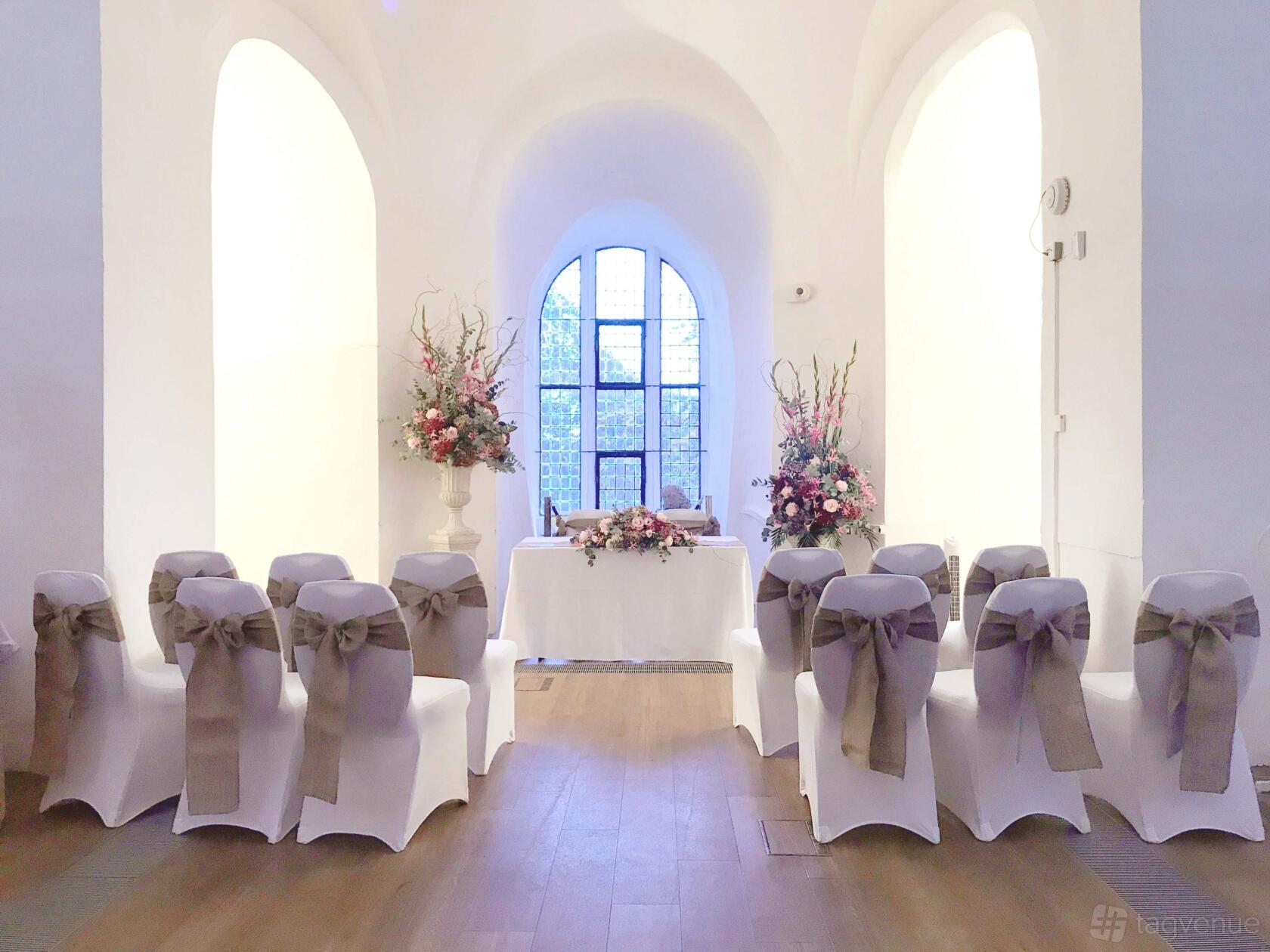 An event space in a museum with arched white walls, wooden floors, and rows of chairs facing a table at Colchester Weddings.