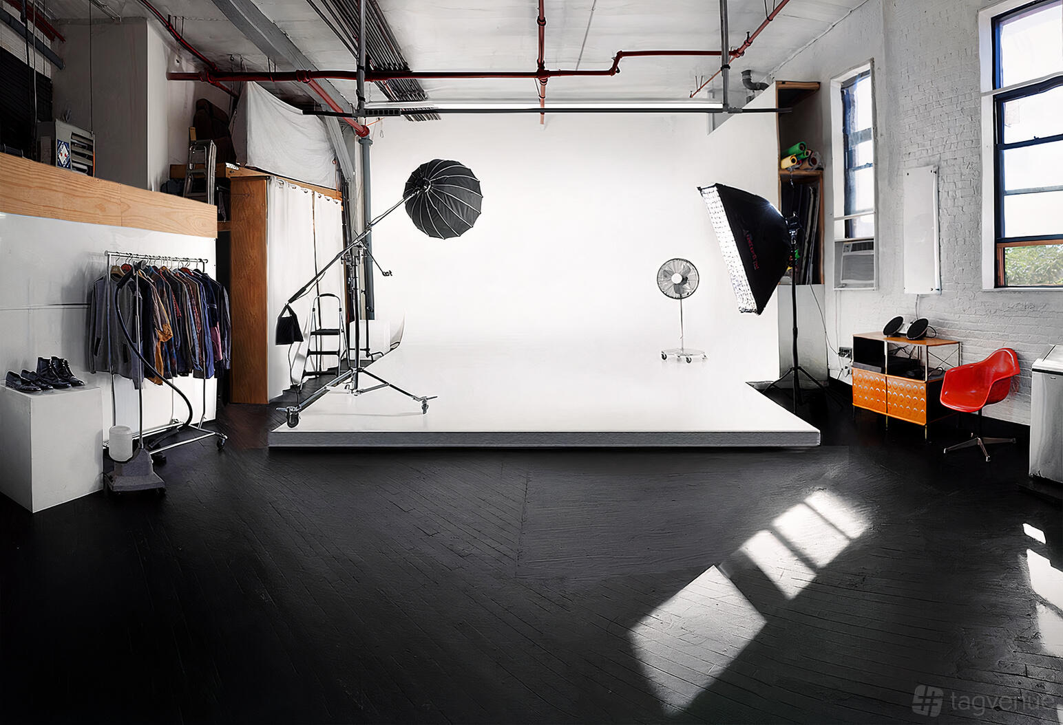 A photo studio with a white cyclorama, lighting equipment, large windows, and clothing racks at Urban Myth Studio.