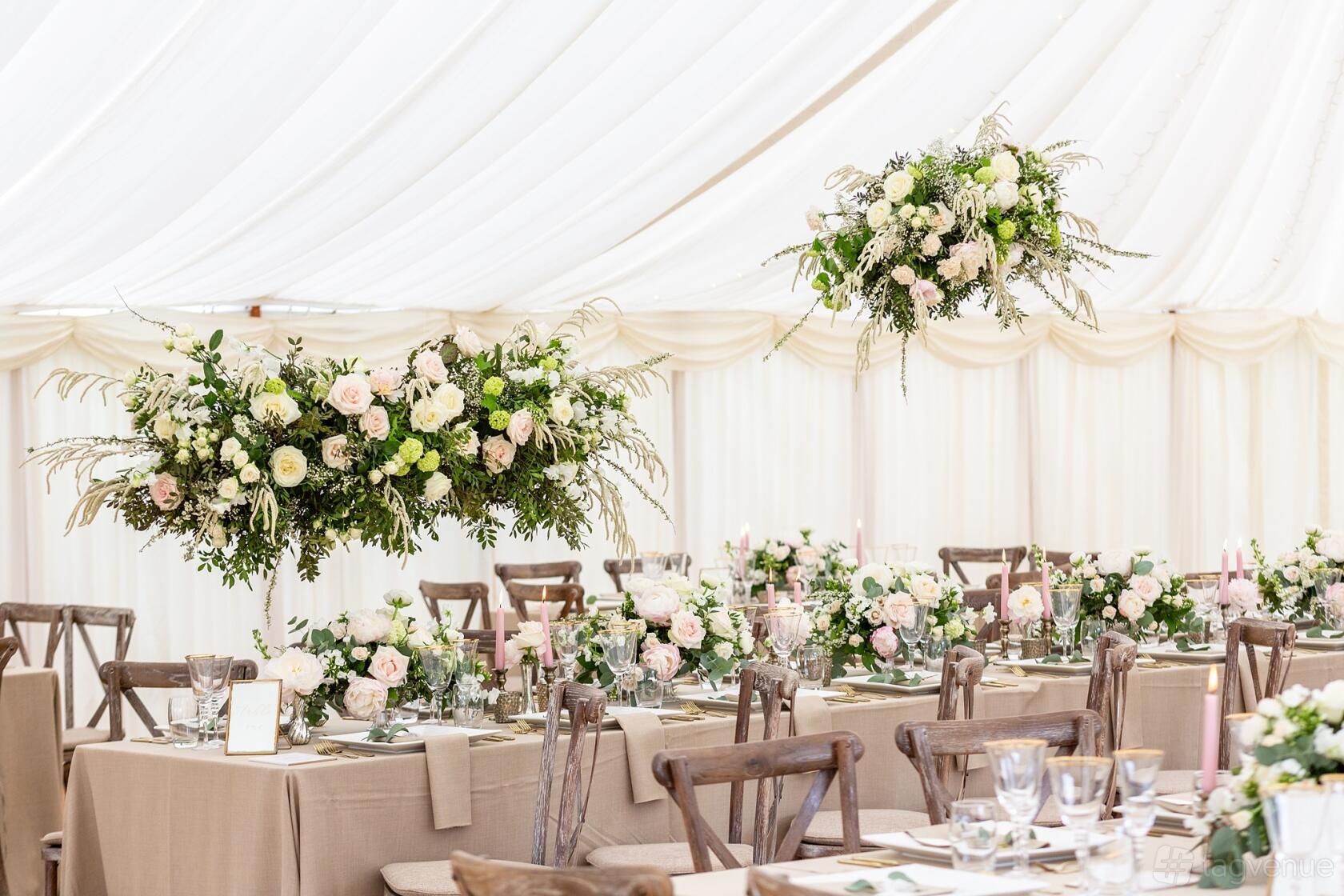An outdoor event space with long tables, wooden chairs, and floral centerpieces under a white marquee at Parish's House.