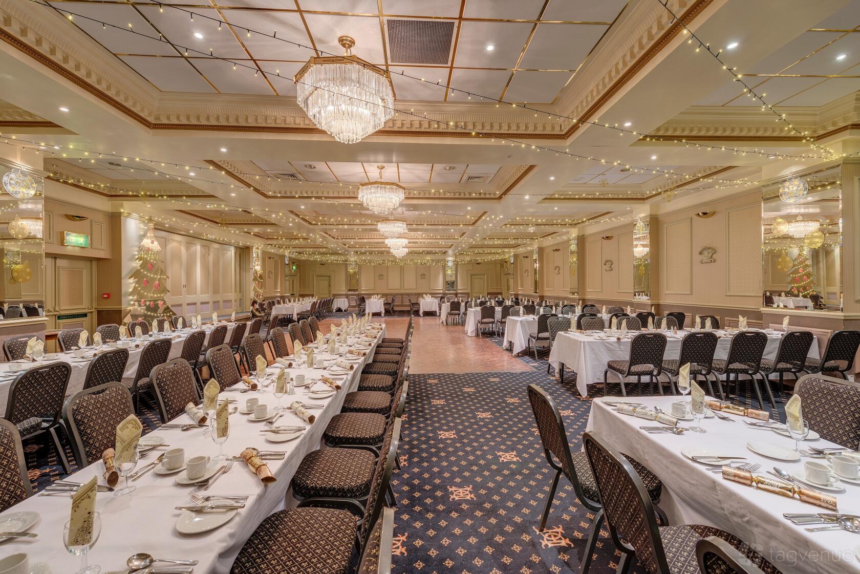 A ballroom with chandeliers, festoon lights, and banquet tables set for dining at The Duke of Cornwall Hotel.