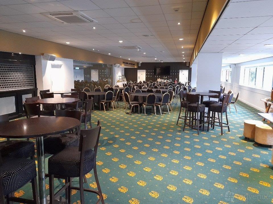 An event space with round tables and chairs, patterned green carpet, and floor-to-ceiling windows at Leicester Tigers.