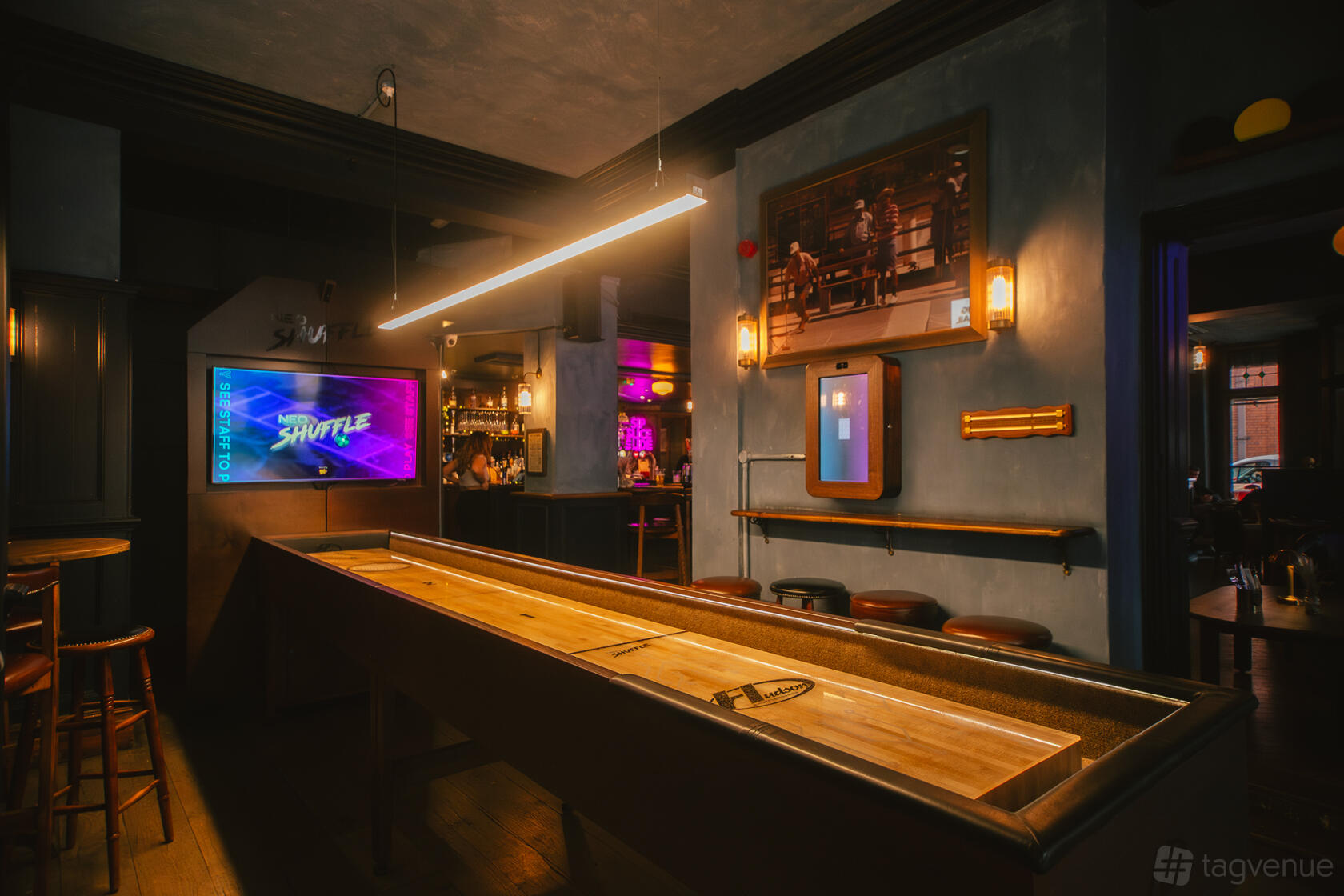 A bar in a pub with a shuffleboard table, warm lighting, and a backlit bar at Newhall Street Tavern.