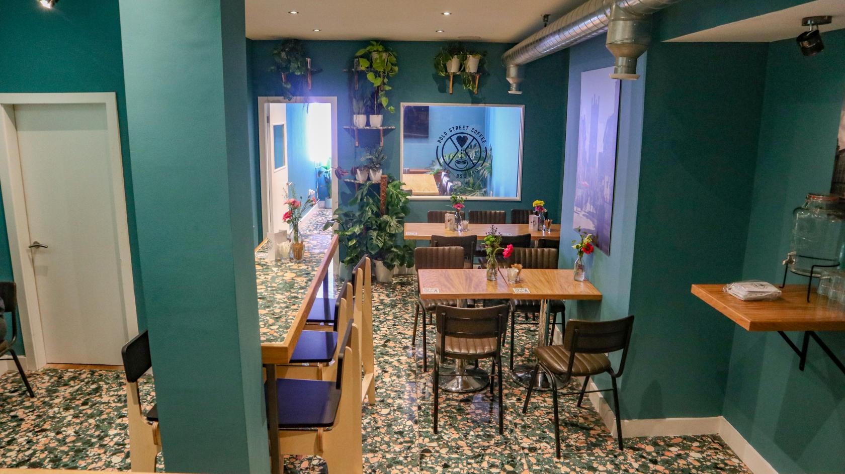 An event space in a cafe with green walls, potted plants, and small wooden tables at Bold Street Coffee Liverpool.