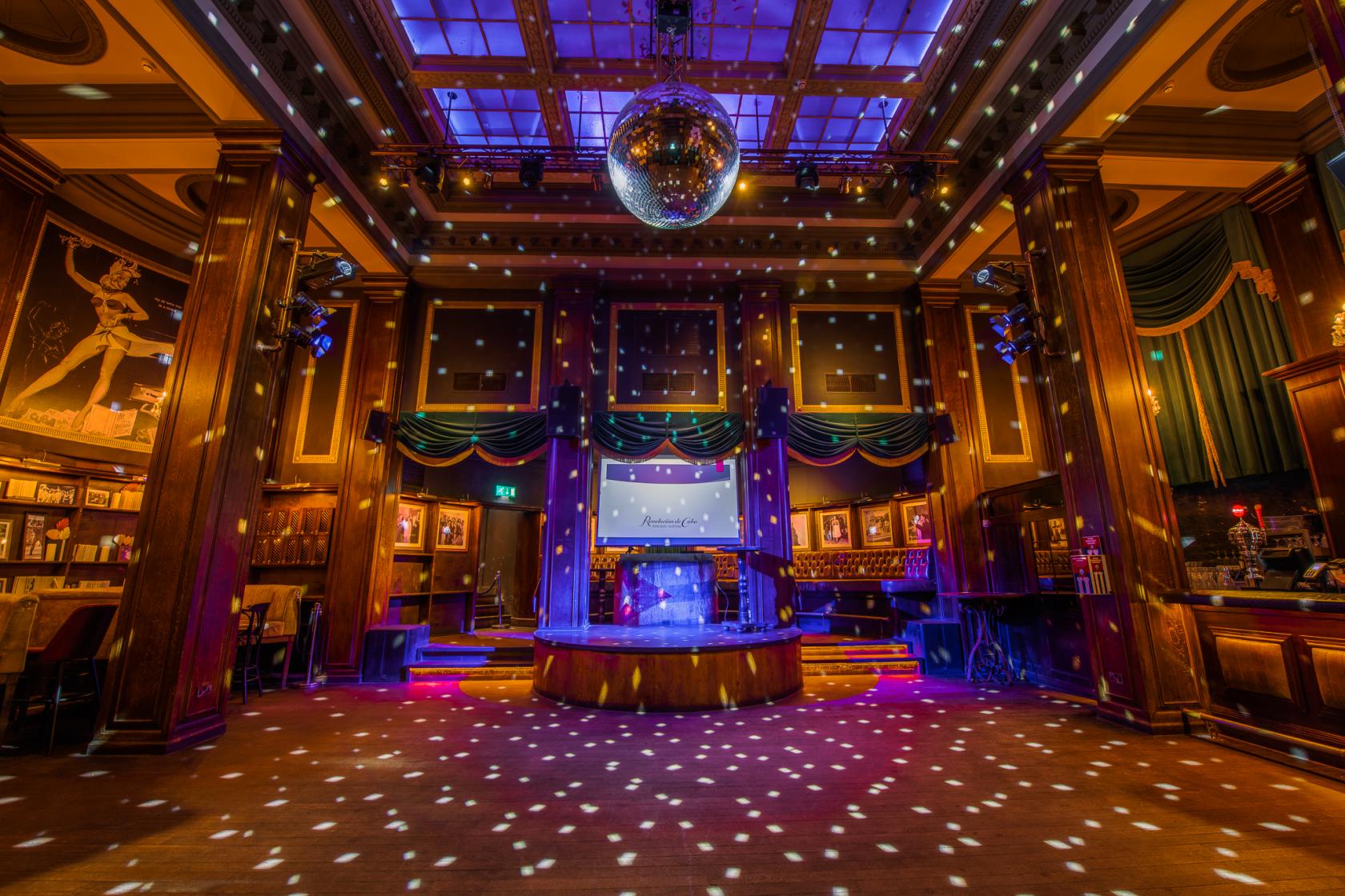 A bar with a large dance floor, disco ball, stage, and wood-paneled walls at Revolucion De Cuba Birmingham.
