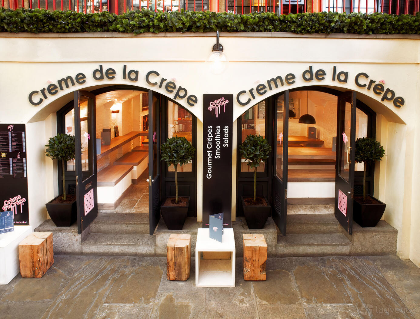 A restaurant entrance with double doors, arched windows, and potted plants at Creme de la Crepe.