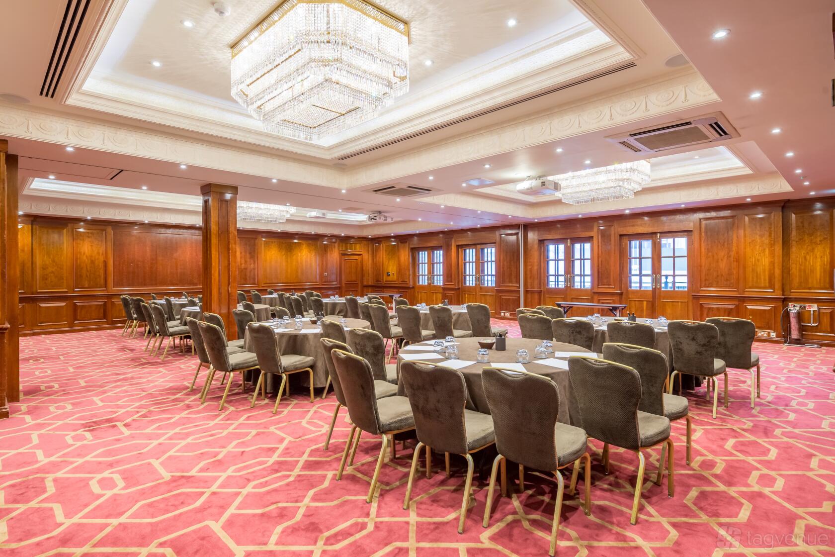 A hotel meeting room with crystal chandeliers, wood-paneled walls, and round tables at Radisson Blu Hotel, London Heathrow.