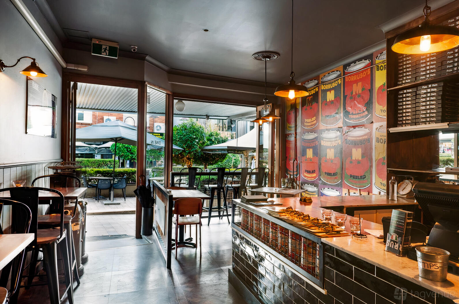 An event space in a restaurant with black tile bar, vintage posters, bistro chairs, and an open entrance at Borruso's Crows Nest.