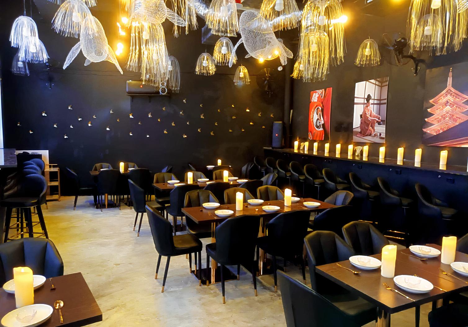 A restaurant with black chairs, candlelit tables, and jellyfish-inspired ceiling lights at SORA.