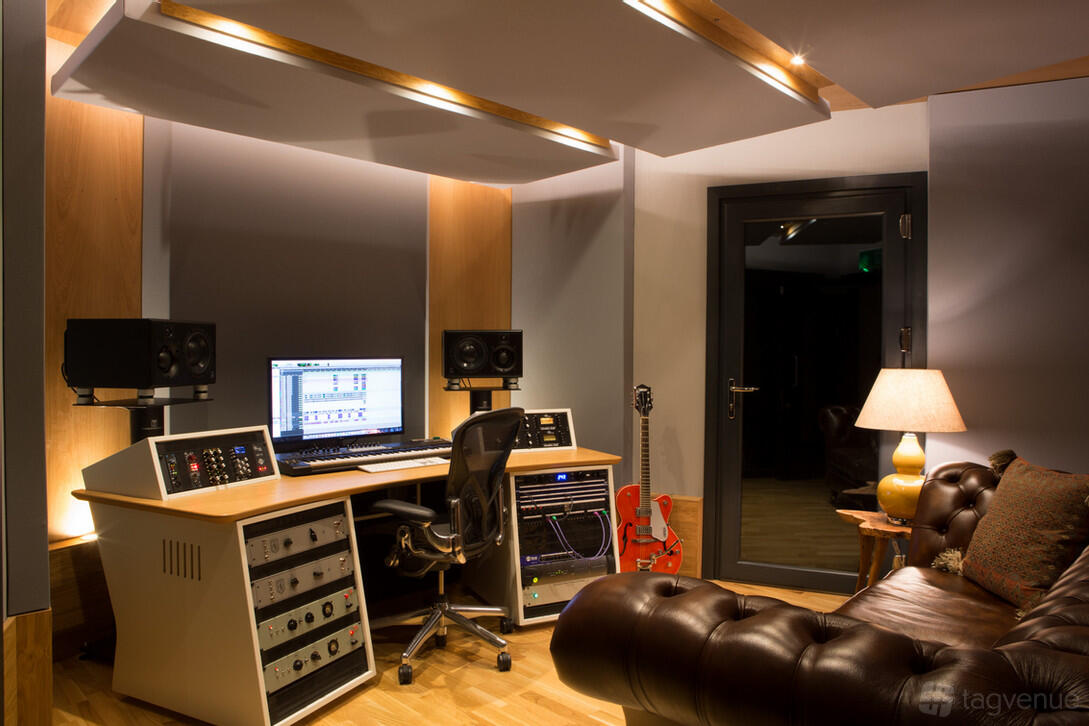 A recording studio with a mixing desk, dual monitors, speakers, and a leather sofa at Dock Street Studios.