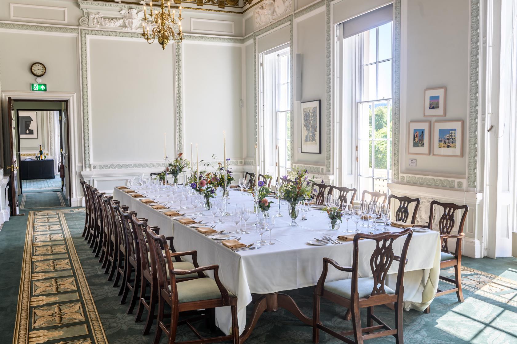 An event venue with high ceilings, tall windows, ornate molding, and a long dining table at {10-11} Carlton House Terrace.