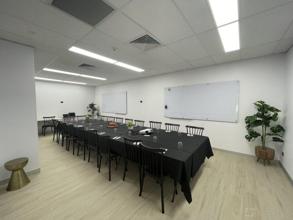 An event venue with rectangular tables covered in black linens, black chairs, whiteboards, and potted plants at Performance Studios Australia.