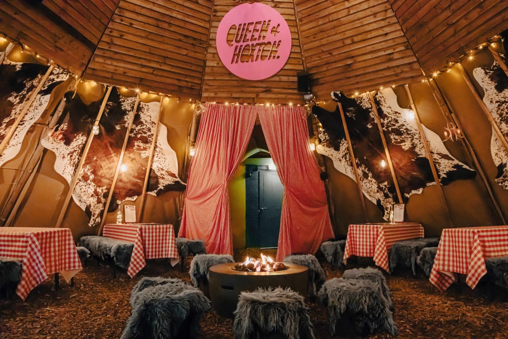A rooftop nightclub with fur-covered stools, red checkered tablecloths, string lights, and a firepit at Queen of Hoxton.