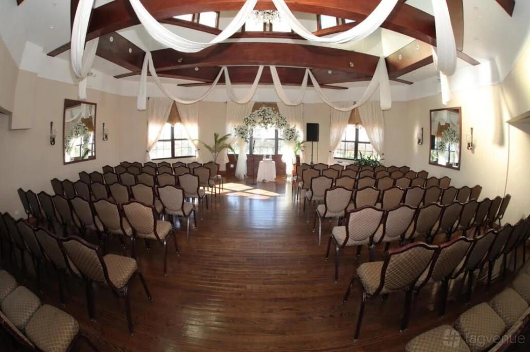 A hall with wood floors, draped ceiling beams, and rows of chairs facing an arbor at The Douglaston Manor.