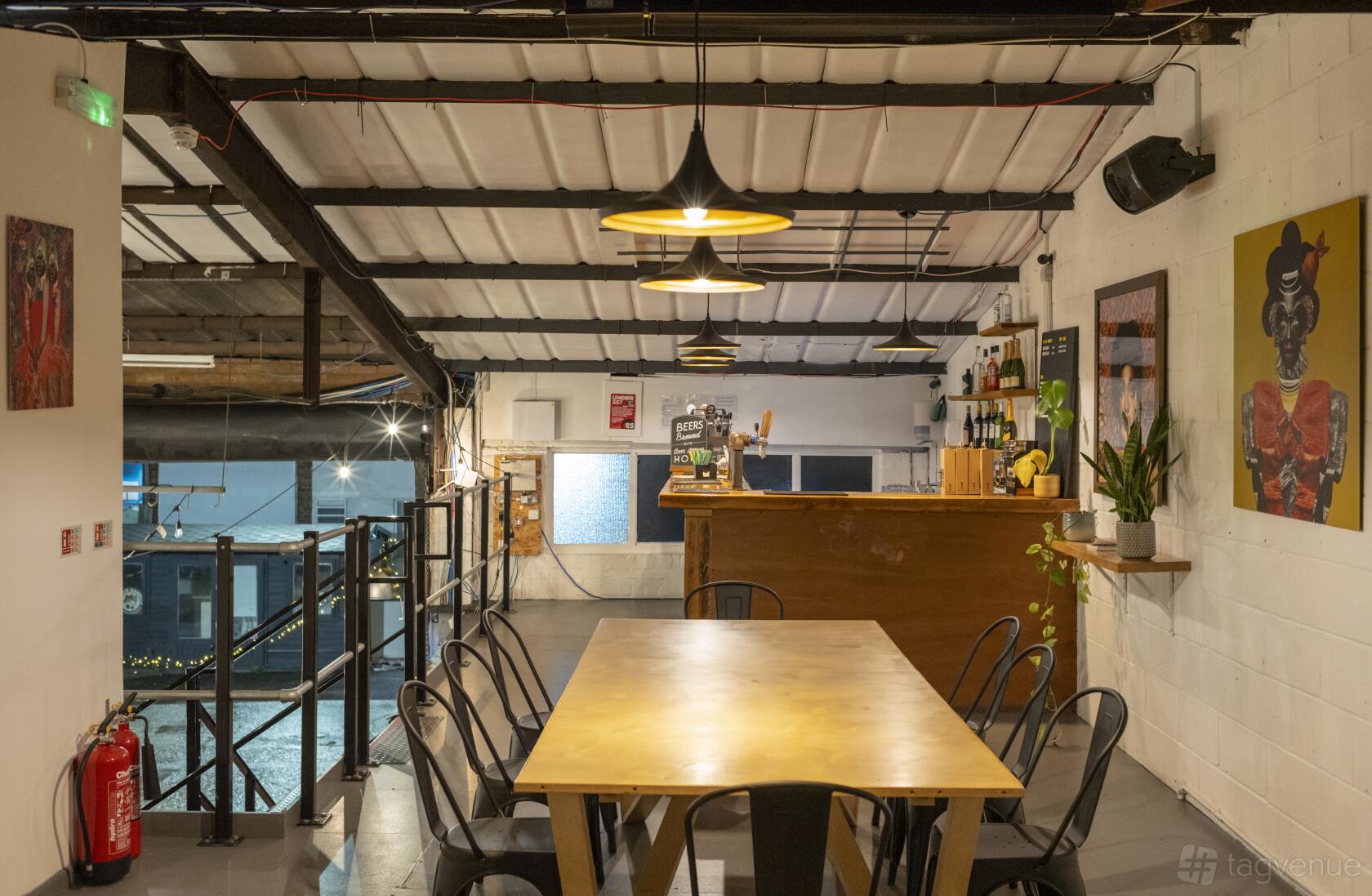 A bar with a wooden communal table, industrial pendant lights, and wall art at Eko Brewery and Tap Room.
