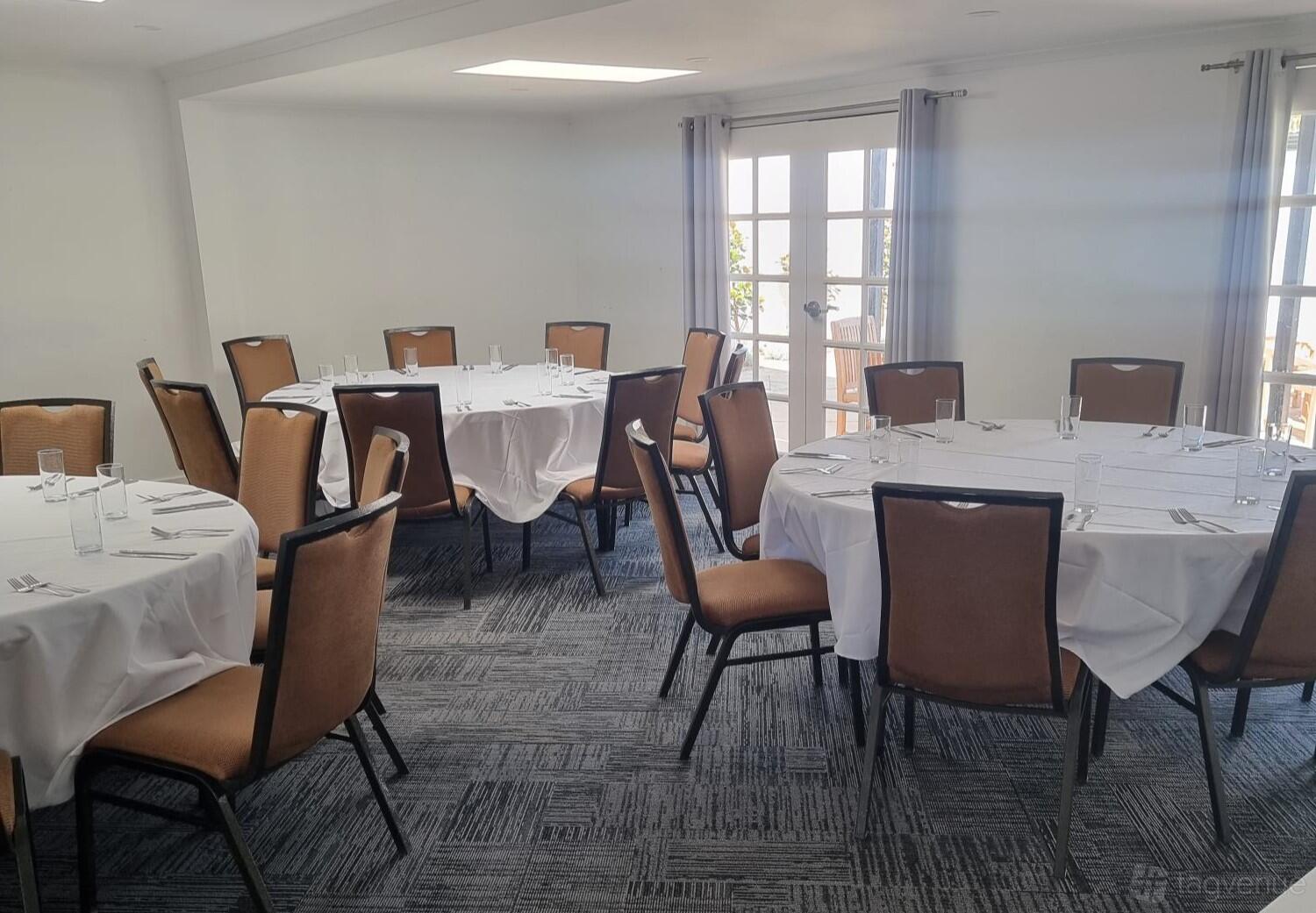 A hotel boardroom with round tables dressed in white linens and natural light at Mercure Gerringong Resort.