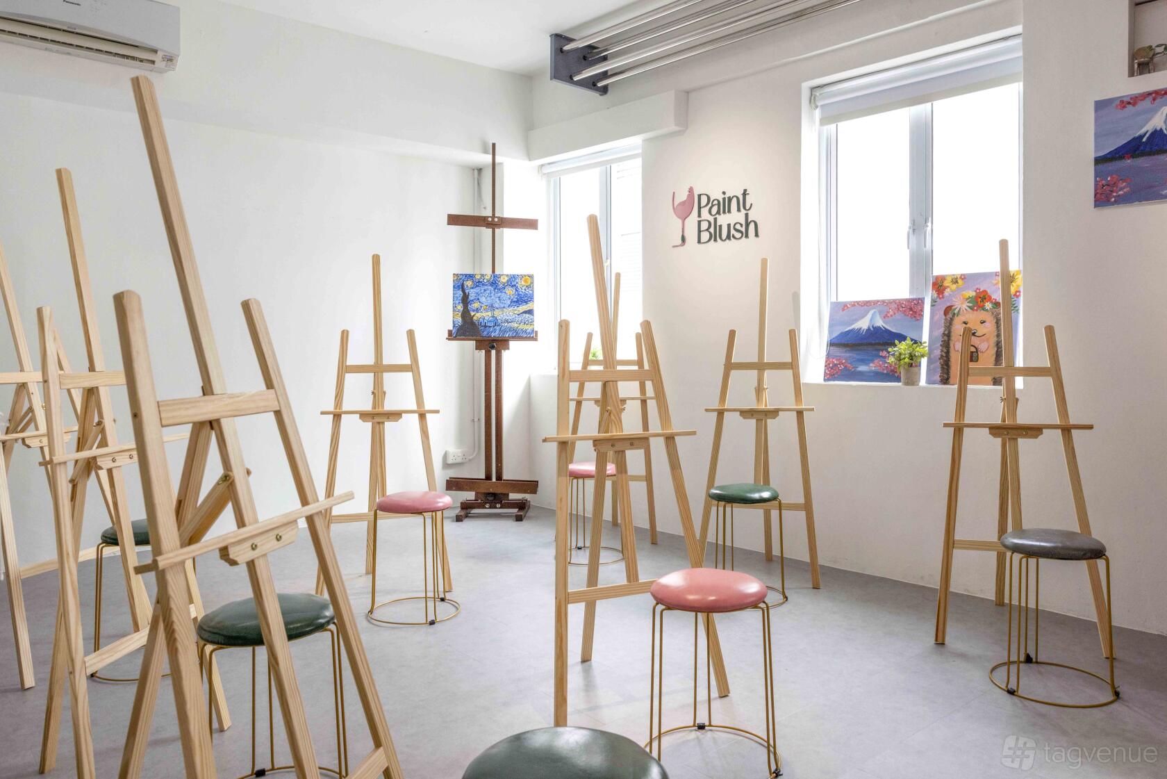 An art studio with wooden easels and colorful stools near large windows at PaintBlush.